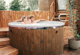 A couple relaxes in a hot tub at The Nutshell tiny house with sauna at Recreation Park Den Blanken, Netherlands.