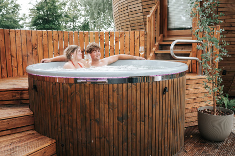 Koppel ontspant in een hot tub bij The Nutshell tiny house met sauna op Recreation Park Den Blanken.