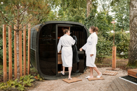 Two people in bathrobes enter an outdoor sauna at The Nutshell tiny house at Den Blanken Recreation Park.