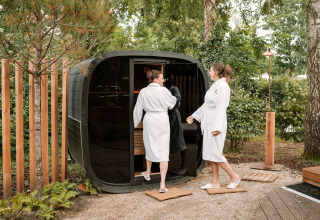 Two people in bathrobes enter an outdoor sauna at The Nutshell tiny house at Den Blanken Recreation Park.