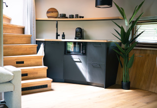 Kompakt køkkenhjørne med moderne sort inventar, trappe, plante og vindue i et tiny house ved Den Blanken.