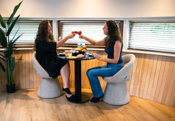 Dos mujeres brindan y disfrutan de una comida en una mesa redonda en una tiny house en Den Blanken, Países Bajos.