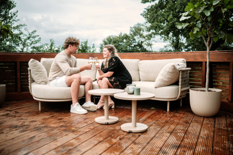 Couple enjoying wine on outdoor sofa at The Nutshell tiny house with hot tub at Den Blanken, Netherlands.
