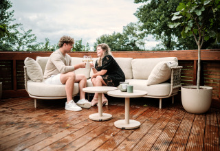 Couple enjoying wine on outdoor sofa at The Nutshell tiny house with hot tub at Den Blanken, Netherlands.