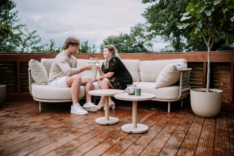 Stel met wijnglazen op terras bij The Nutshell, een tiny house met hottub in Den Blanken, Nederland.