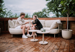 Par nyder et glas vin på en udendørs terrasse med sofa på The Nutshell ved Den Blanken i Holland.