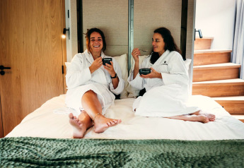 Zwei Frauen im Bademantel frühstücken auf einem Bett im Tiny House The Nutshell im Den Blanken Park.