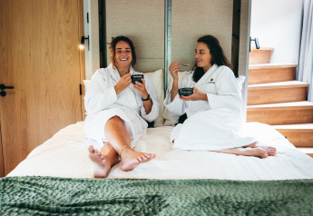 Deux femmes en peignoirs prennent le petit-déjeuner sur un lit à The Nutshell tiny house, Den Blanken, Pays-Bas.