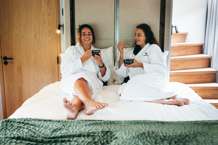 Dos mujeres en albornoces disfrutan desayuno en la cama en The Nutshell tiny house en Den Blanken, Países Bajos.
