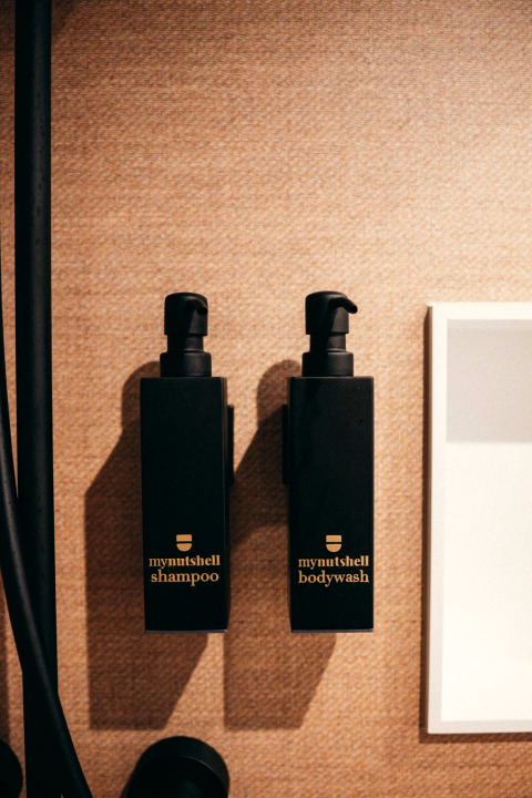 Two black bottles labeled 'mynutshell shampoo' and 'mynutshell bodywash' mounted on a bathroom wall.