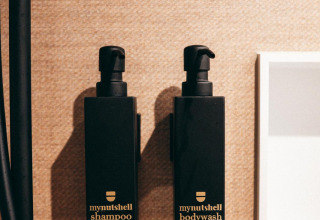 Twee zwarte flacons met opschrift 'mynutshell shampoo' en 'mynutshell bodywash' aan een badkamerwand.