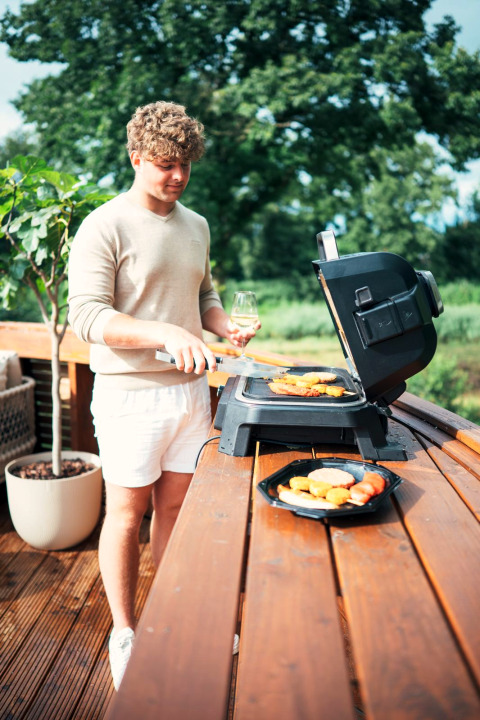 A man grills food on a deck at a tiny house with hot tub and sauna at Recreation Park Den Blanken, Netherlands.