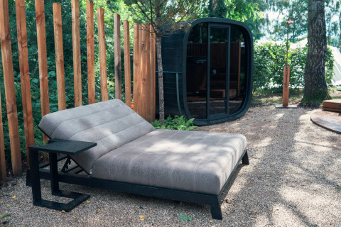 Modern outdoor relaxation area with lounge chair, sauna hut, and wood fence at Den Blanken, Netherlands