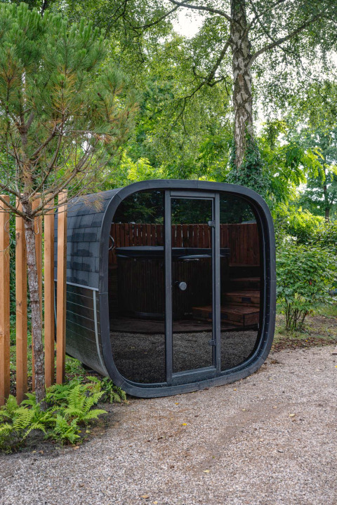 Modern, rounded black sauna at The Nutshell in Recreation Park Den Blanken, Netherlands, amid greenery.