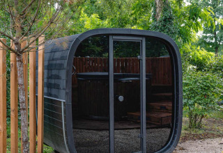 Modern, rounded black sauna at The Nutshell in Recreation Park Den Blanken, Netherlands, amid greenery.