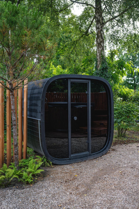 Eigentijdse, afgeronde zwarte sauna bij The Nutshell in Recreatiepark Den Blanken, Nederland, in het groen.