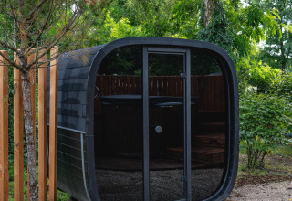 Moderne, sort, rund sauna ved The Nutshell i Recreatiepark Den Blanken, omkranset af grønne træer.