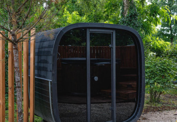 Sauna moderna nera e arrotondata a The Nutshell nel Recreation Park Den Blanken, Paesi Bassi, tra il verde.