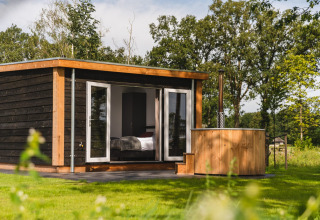 Moderne tiny house met houten hot tub op grasveld bij Vakantiepark Hölte in Nederland, omringd door natuur.