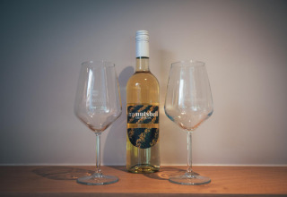 Een fles witte wijn met twee wijnglazen op een plank in een tiny house The Nutshell in Nederland.