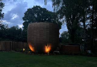 Unikt træhytte, kaldet The Nutshell, med oplyst facade, omgivet af grønt ved Den Blanken i Holland.