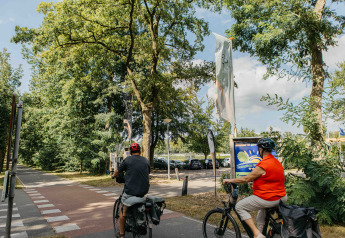 Due ciclisti vicino all'ingresso del parco ricreativo Den Blanken nei Paesi Bassi, circondati da alberi.