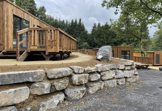 Modern wooden lodges with stone retaining wall, nestled among trees and greenery in a serene forest setting.