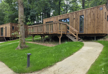 Moderne træhytter i en skov, med grønne græsplæner, gangsti og terrasse, perfekt til lodgestemning.