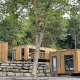 Modern wooden lodge cabins set on a wooded hillside, surrounded by lush green trees and stone walls.