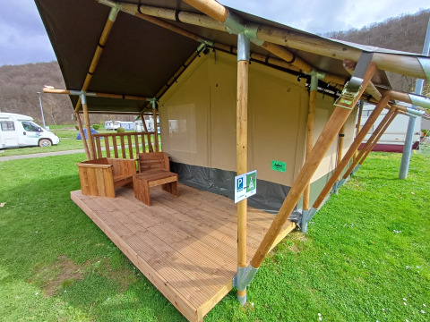 Safari-Zelt mit Holzveranda und Gartenmöbeln auf einem Campingplatz, Wohnmobile im Hintergrund.