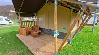 Tenda safari con veranda in legno e mobili da esterno su un campeggio, camper sullo sfondo.