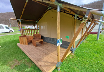 Tente safari avec véranda en bois et mobilier d'extérieur sur un camping, camping-cars en arrière-plan.