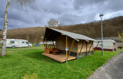 Safarizelt auf Camping la Roche in Belgien, mit Holzterrasse, umgeben von Wohnmobilen und Bäumen.
