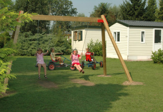 Børn leger på gynger og pedalbiler foran mobile homes i en feriepark i Gelderland, Holland, på en solskinsdag.