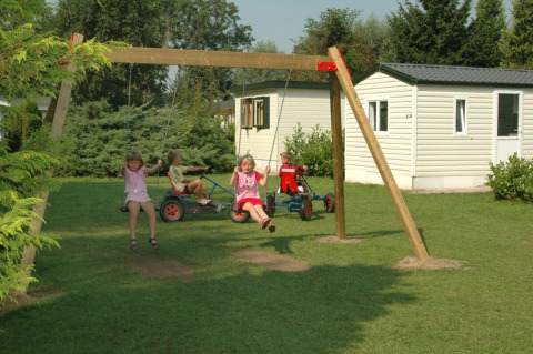 Niños juegan en columpios y karts de pedales frente a casas móviles en un parque de vacaciones en Gelderland, Países Bajos.