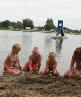 Kinderen spelen in het zand bij het water in Recreatiepark de Scherpenhof, met caravans op de achtergrond.