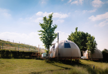 Panorama Dome au Camping Vinkenhof aux Pays-Bas avec tentes dôme, arbres et ciel bleu en arrière-plan.