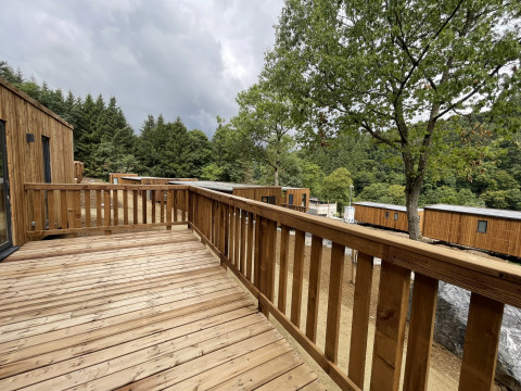 Wooden deck at a lodge with a view of cabins, trees, and forested hills under a cloudy sky.