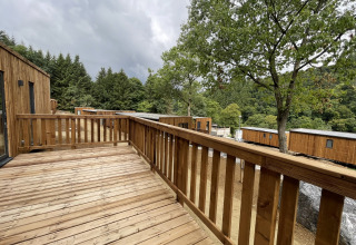 Wooden deck at a lodge with a view of cabins, trees, and forested hills under a cloudy sky.