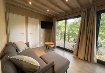Knusse woonkamer in een lodge met zetel, salontafel, tv en schuifdeuren naar een terras met boszicht.