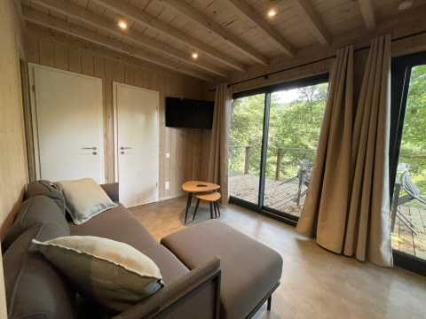 Gemütliches Lodge-Wohnzimmer mit Sofa, Couchtisch, TV und Zugang zur Terrasse mit Waldblick.