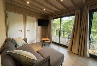 Gemütliches Lodge-Wohnzimmer mit Sofa, Couchtisch, TV und Zugang zur Terrasse mit Waldblick.