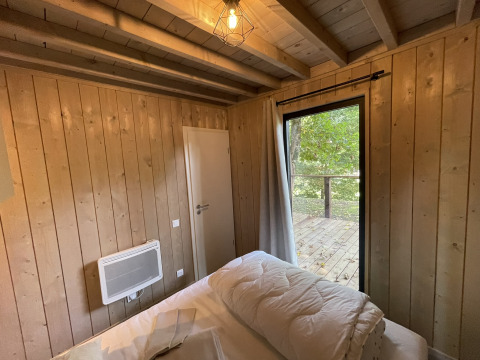 Cozy lodge room with wooden walls, bed, electric heater, white door, and view of deck and green forest.