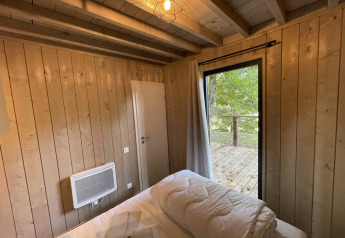 Gemütliches Holzzimmer in einer Lodge mit Bett, Heizung, Tür und Blick auf eine Holzterrasse und Bäume.
