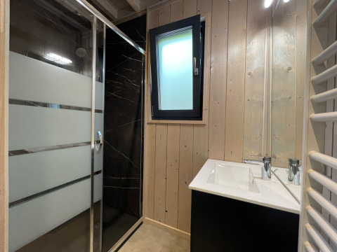 Modernes Badezimmer in einer Lodge mit schwarzer Dusche, Glaswand, Holzverkleidung und kleinem Fenster.