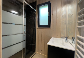 Moderne badeværelse i en lodge med sort bruser, glasdør, træpaneler og et lille vindue og vask.
