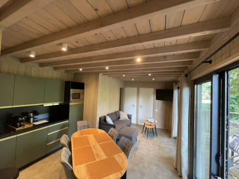 Accogliente interno di lodge con soffitto in legno, cucina moderna, tavolo da pranzo, divano e ampie finestre.