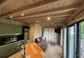 Indbydende interiør af en lodge med træloft, moderne køkken, spisebord, sofa og store vinduer.