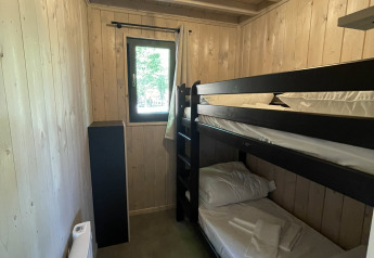 Kleine kamer in een lodge met houten muren, een stapelbed, venster, radiator en bedlinnen.