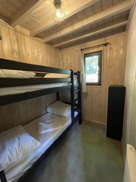 Small lodge bedroom with wooden bunk beds, light wood-paneled walls, a window, and minimalist decor.